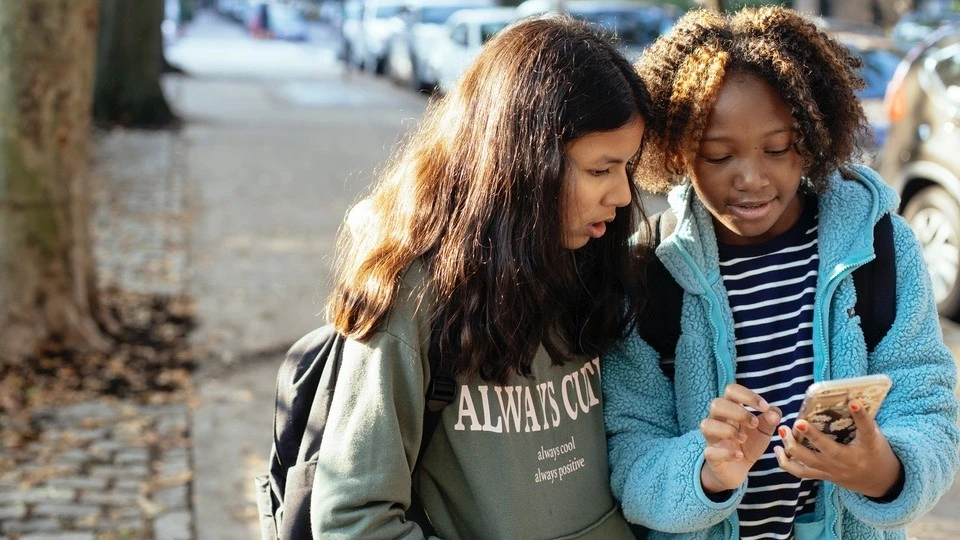 Two children engrossed in using a mobile phone together on a sunlit city street, reflecting the importance of online safety in everyday life.