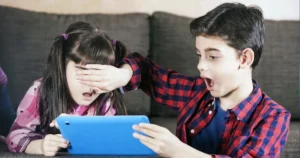 A young girl covers her eyes with her hand, looking upset, while a boy next to her expresses shock at what they see on the tablet, highlighting the need for discussions on cyberethics for our kids.