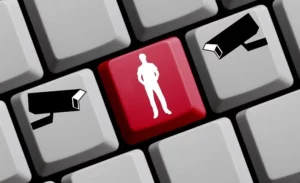 An illustration of a computer keyboard with a striking red key in the center that features the silhouette of a person. On adjacent keys to the left and right, there are icons of surveillance cameras pointed towards the central figure. This image metaphorically represents the delicate balance between 'monitoring vs. spying' in the context of ensuring online safety and privacy.