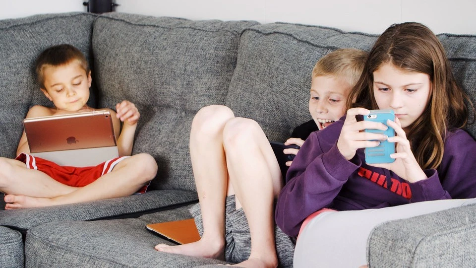 Three children sitting on a sofa using their smartphones