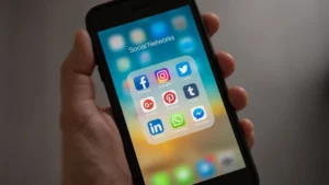 A person's hand holding a smartphone with a display showing various social media app icons, representing the critical theme of the blog article "Social Media vs. Reality: 3 Ways to Encourage Positive Online Experiences.
